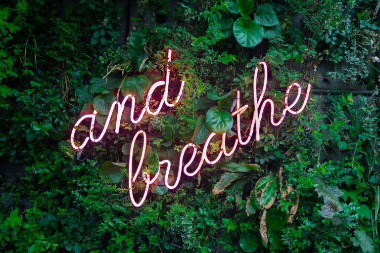 neon sign read "and breath" on a leafy background.