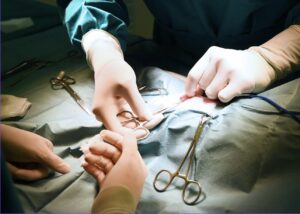 Cloeup of two pairs of hands performing surgery. One hand is tying a suture, surrounded by surgical tools.